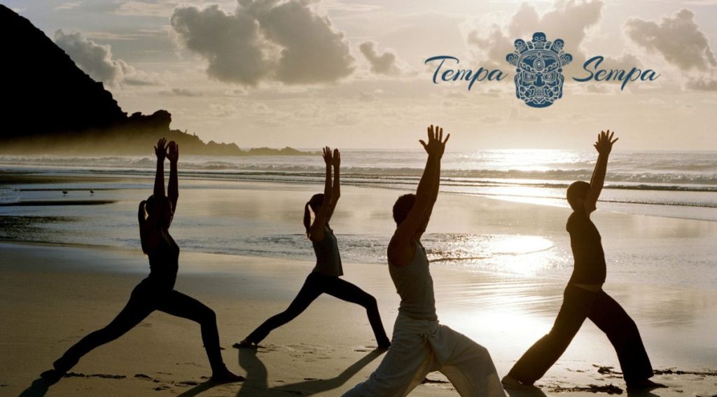personas haciendo yoga enla playa a la salida del sol